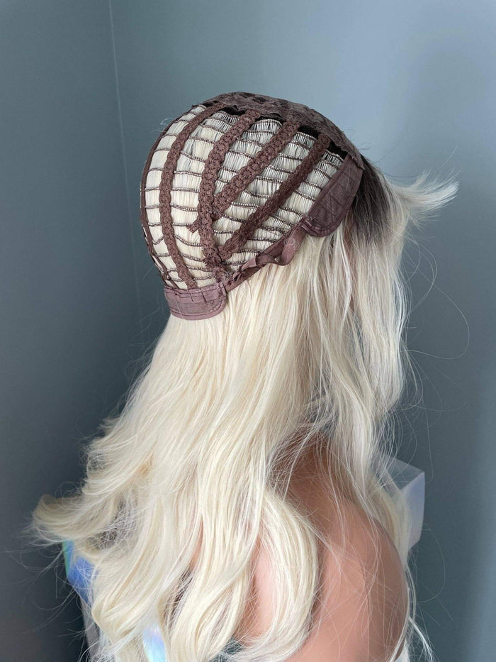 Person with long blonde hair wearing a brown and beige mesh cap against a gray background