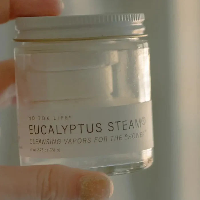 Jar of 'Eucalyptus Steam' product held by a hand with a neutral background