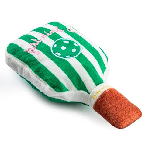 The HAUTE DIGGITY DOG GREEN STRIPED PICKLEBALL PADDLE DOG TOY is a squeaky plush toy shaped like a green pickleball paddle with a brown handle, featuring a white pickleball and "dink responsibly" embroidered on its surface—perfect for playful pups who love pickleball!.
