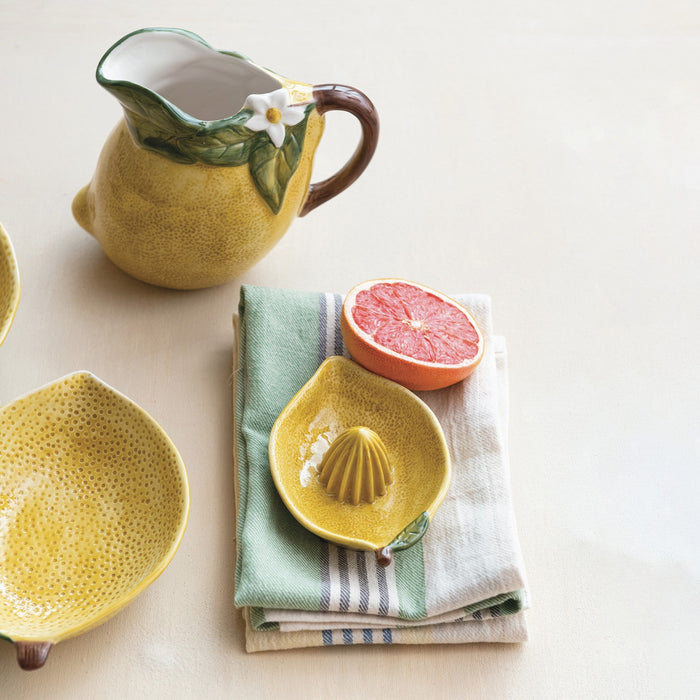 The CREATIVE COOP HAND-PAINTED STONEWARE LEMON SHAPED JUICER features a textured yellow finish, brown stem, and green leaf—ideal as a rustic squeezer and farmhouse kitchen decor. Shown in top and side views.