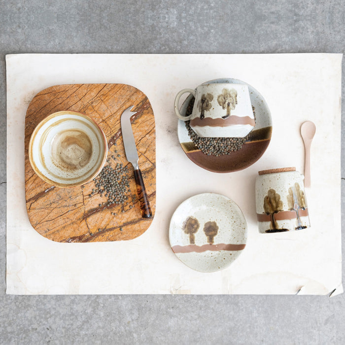 The HAND-PAINTED STONEWARE MUG WITH TREES by CREATIVE COOP is a beige stoneware mug with a large handle, wavy brown stripe, and two stylized tree designs, perfect for adding rustic charm to your coffee routine.