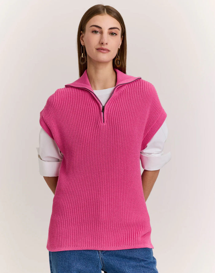 A woman with straight brown hair wears the HINSON WU BROOKE Sleeveless Knit Vest in bright pink over a white shirt and blue jeans, standing against a plain light background.