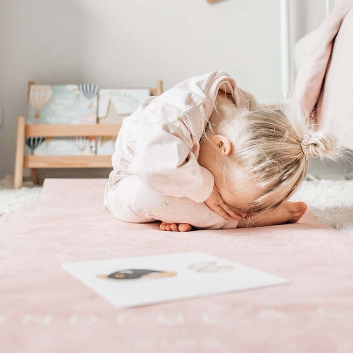 Child lying on a bed with a pink blanket and white wall in the background