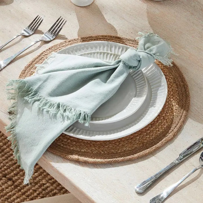 The NAPA HOME AND GARDEN - JUTE COIL ROUND PLACEMAT features a braided jute texture and natural beige color, resembling a hand-woven placemat, shown against a white background.