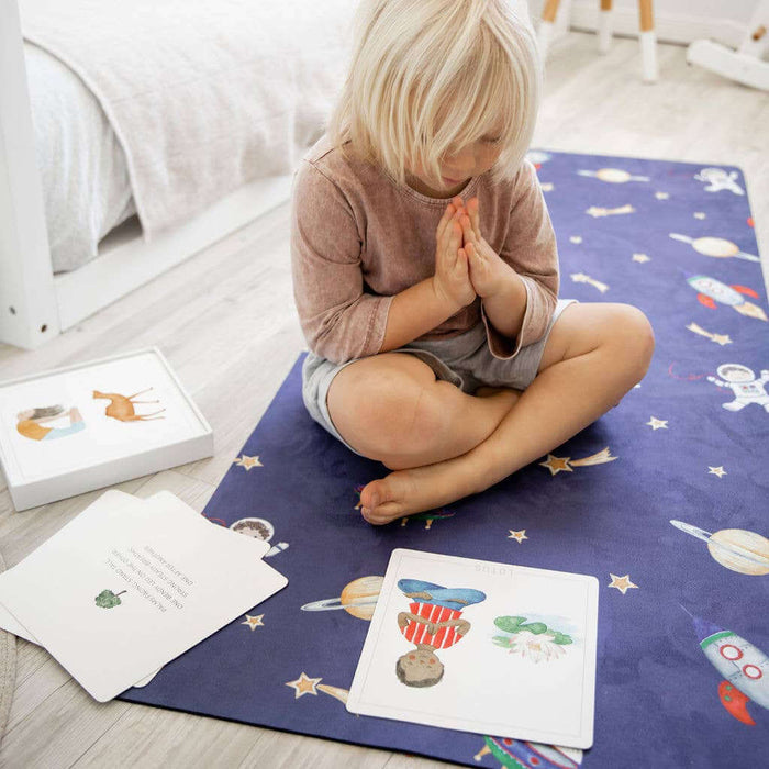Child sitting on a colorful mat with space-themed illustrations in a bright room.