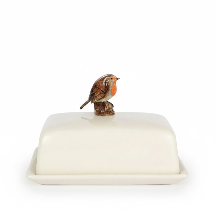 The QUAIL CERAMICS - ROBIN BUTTER DISH by QUAIL DESIGNS is a white ceramic butter dish with a lid, topped with a hand-painted robin figurine, displayed against a plain white background.