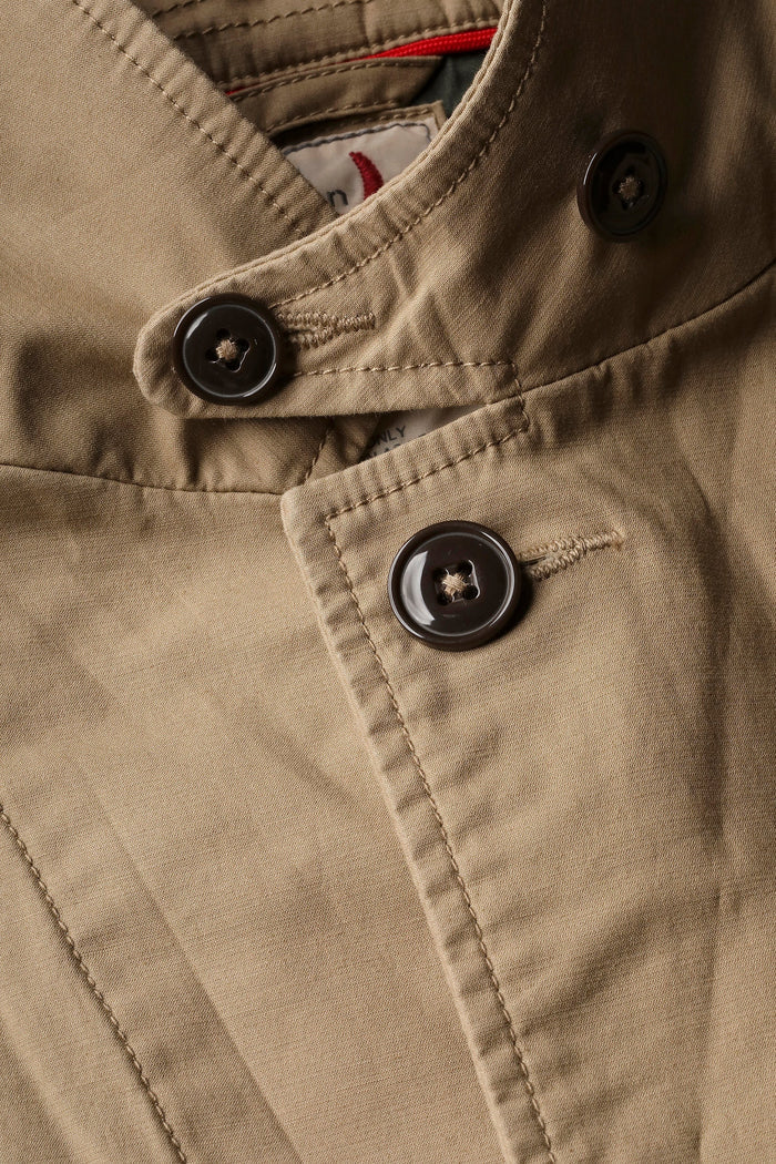 A person wears the RELWEN Flyweight Flex Blazer in British Khaki over a blue and white checkered shirt with green pants, standing hands-in-pockets against a white background. Face not visible.