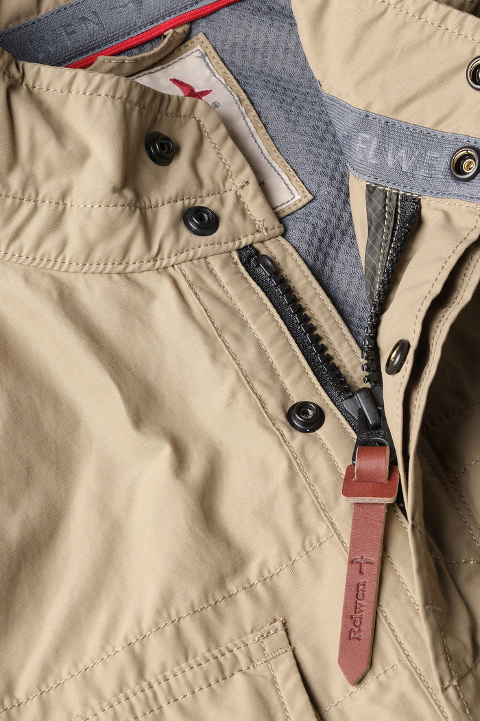 A person wearing the RELWEN Sailcloth Tanker in Desert Khaki stands on a wooden walkway, hands in pockets, with trees and sunlight in the background.
