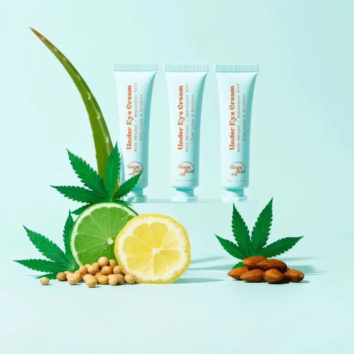 Three tubes of Under Eye Cream with cannabis leaves, lime, lemon, and almonds on a light blue background.