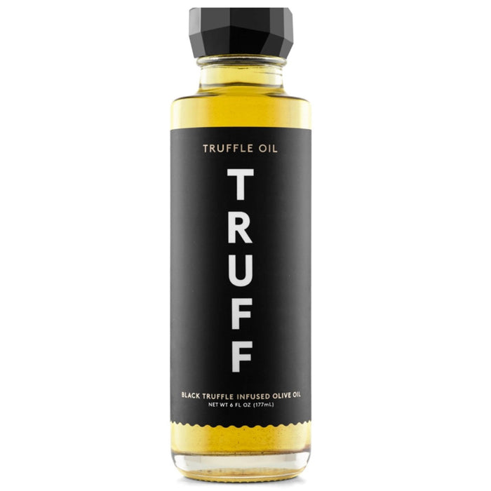 A tall, transparent glass bottle of TRUFF HOT SAUCE truffle oil with a black hexagonal cap. The label is black with "Truffle Oil" written at the top and "TRUFF" in large white vertical letters. The label also states "Black Winter Truffle Infused Olive Oil" and the net weight of 6 fl oz (177ml).