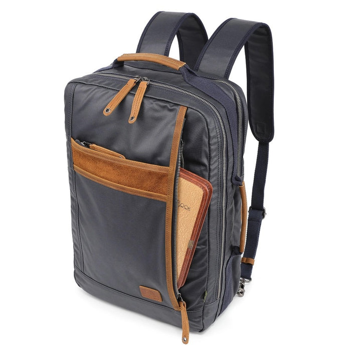 The TSD BRAND - MADRONE COATED CANVAS BACKPACK IN NAVY features brown leather accents, a spacious main compartment, a padded laptop sleeve with snap closure, and multiple zippered pockets on the inside flap.