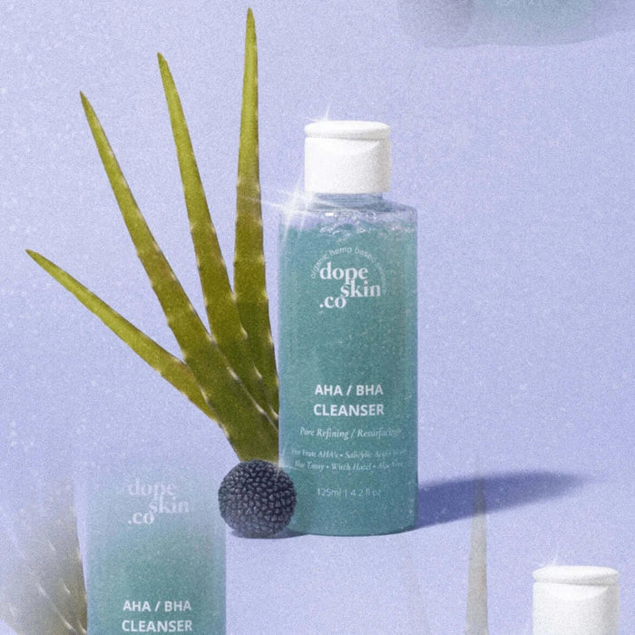 Bottle of 'dope skin co' AHA/BHA Cleanser with aloe vera leaves on a light blue background