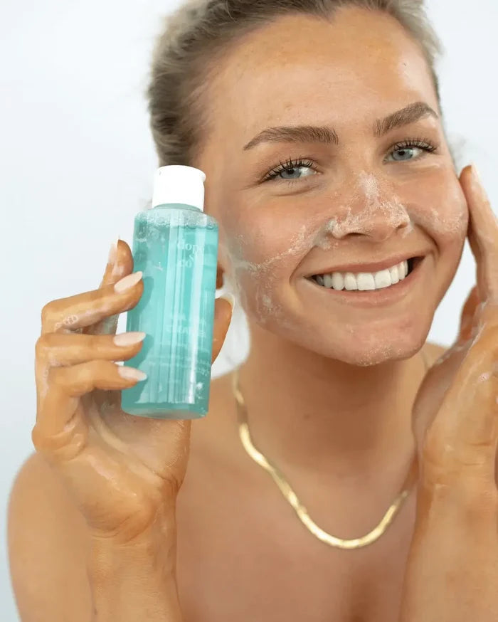 Woman applying a facial cleanser with a bottle of blue cleanser in her hand.
