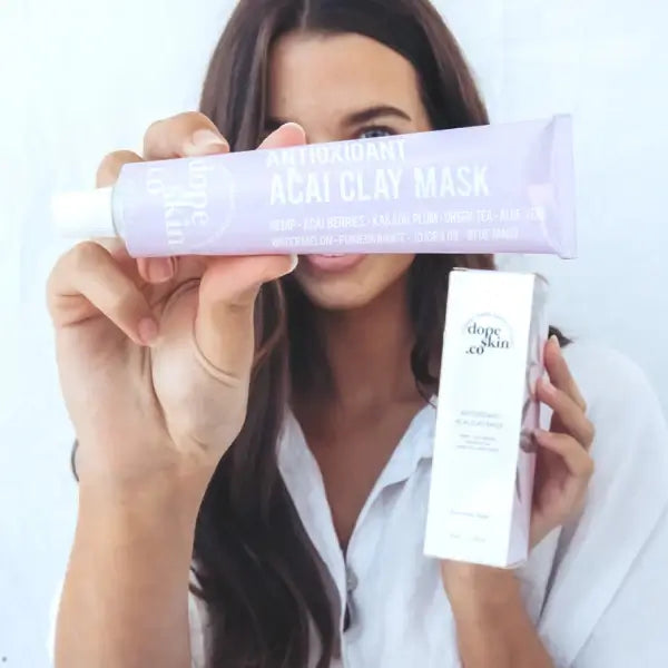 Woman holding an antioxidant acai clay mask and a skincare product with a plain background