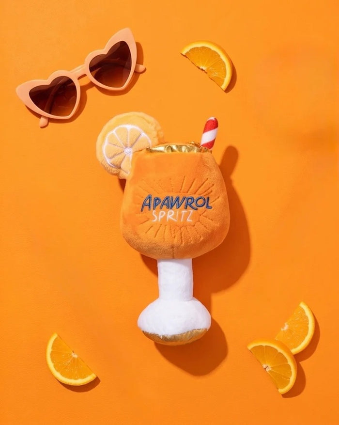 The HAUTE DIGGITY DOG APAWROL SPRITZ DOG TOY is a plush, squeaky dog toy shaped like an orange cocktail glass, featuring "APAWROL SPRITZ" embroidery, a slice of orange on top, and a red-striped straw.