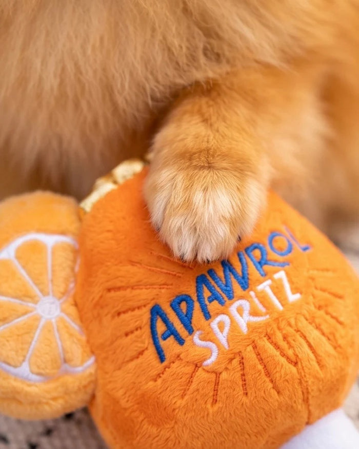 The HAUTE DIGGITY DOG APAWROL SPRITZ DOG TOY is a plush, squeaky dog toy shaped like an orange cocktail glass, featuring "APAWROL SPRITZ" embroidery, a slice of orange on top, and a red-striped straw.