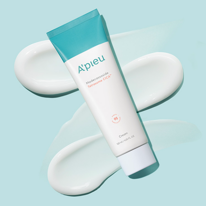 A'pieu Madecassoside Tetrasome Cica Cream in a white tube with blue accents, alongside a spoonful of the cream and a few leaves of Centella Asiatica.