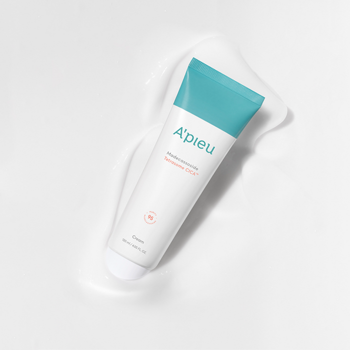 Overhead studio shot of the white tube of A'pieu Madecassoside Sensitive Cica Cream with a teal cap, lying in a pool of its own white, creamy product. The image highlights the rich, comforting texture of the Madecassoside cream for soothing sensitive and irritated skin and promoting skin barrier repair.