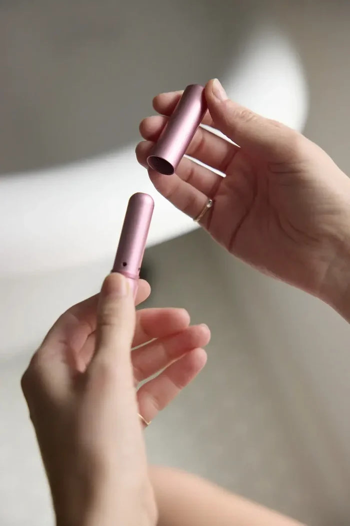 Two hands holding pink cylindrical objects against a neutral background