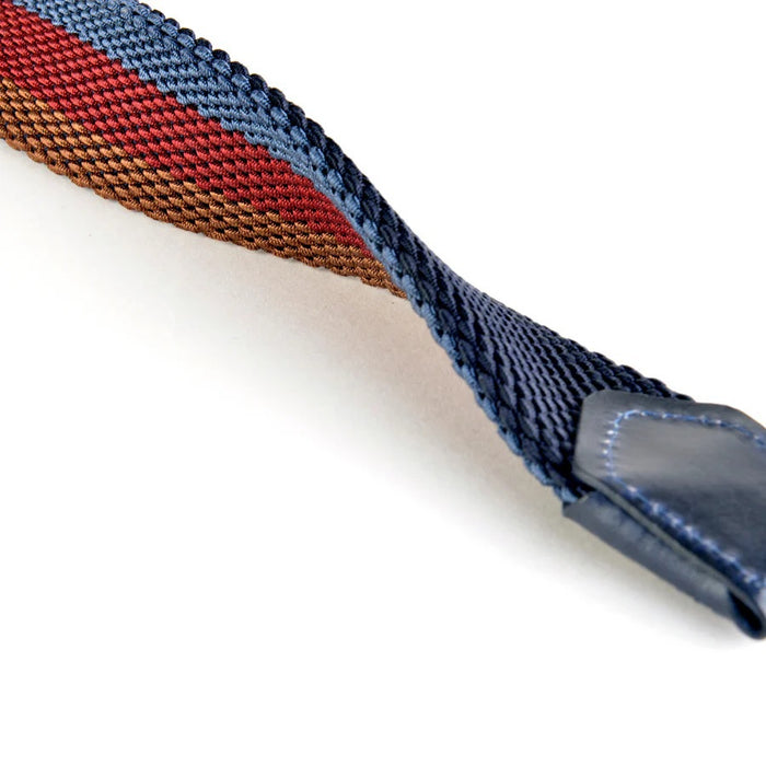 A close-up of the ATHISON Reversible Stretch Belt in navy, khaki, and white stripes with a silver buckle and navy leather details, shown on a light wooden surface; reverses to solid navy.