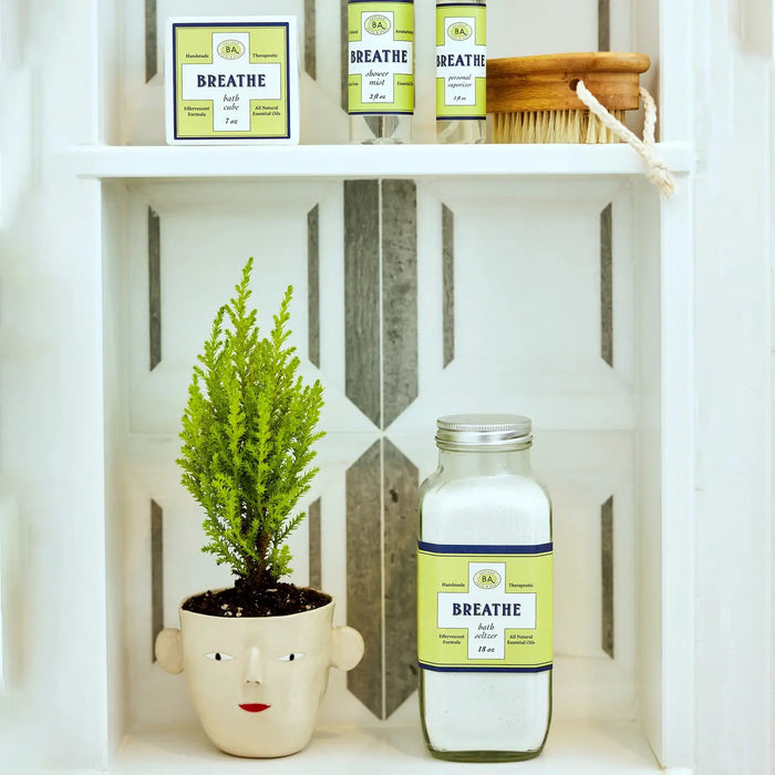 The BAUDELAIRE - BREATHE BATH SELTZER is a handmade 18 oz glass bottle with a yellow/green label, featuring an effervescent formula infused with eucalyptus and all-natural essential oils for a refreshing bath experience.