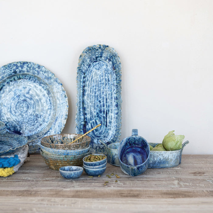 The CREATIVE COOP BLUE STONEWARE ORGANIC-SHAPED PLATTER features a wavy, textured edge and is shown from top and side angles. Its hand-crafted appeal is enhanced by a reactive crackle glaze in blue with white accents.