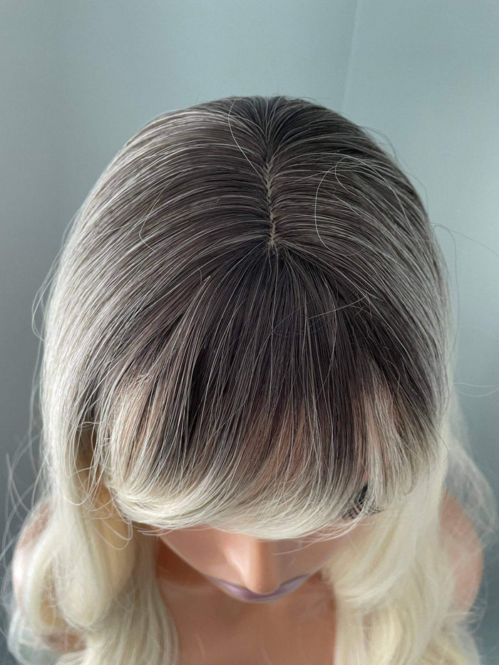Blonde wig with a gray root on a mannequin head against a light blue background