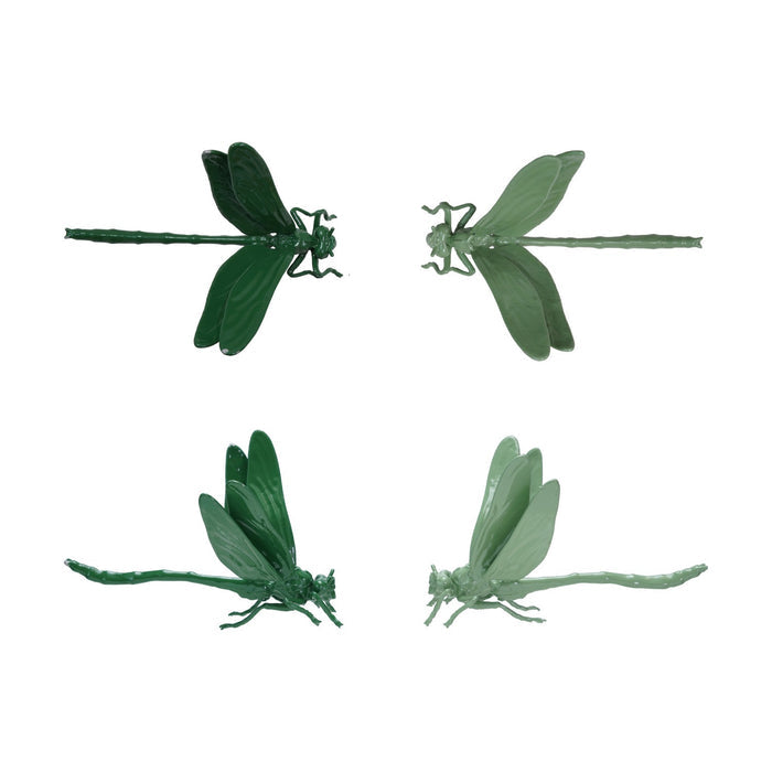A pop-up book on a wooden surface showcases two large green CAST IRON DRAGONFLY sculptures by CREATIVE COOP, emerging from its pages against a plain light background.