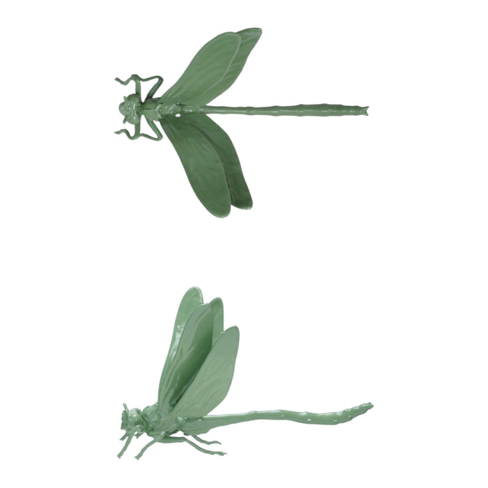 A pop-up book on a wooden surface showcases two large green CAST IRON DRAGONFLY sculptures by CREATIVE COOP, emerging from its pages against a plain light background.