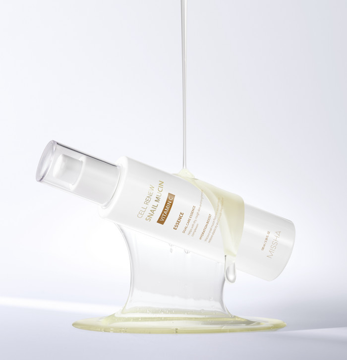 Studio shot of the Missha Cell Renew Snail Mucin Vitamin C Essence bottle tilted, held up by a visible stream of the thick, viscous serum that highlights the snail mucin ingredient's texture for intense skin repair and anti-aging.