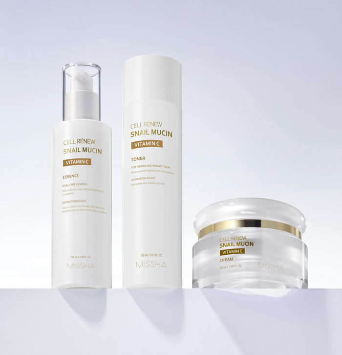 Display of the complete Missha Cell Renew Snail Mucin Vitamin C skincare line: the Ampoule/Essence, the Toner, and the Cream. The products are placed on a sleek white shelf, promoting a full anti-aging and skin brightening regimen.