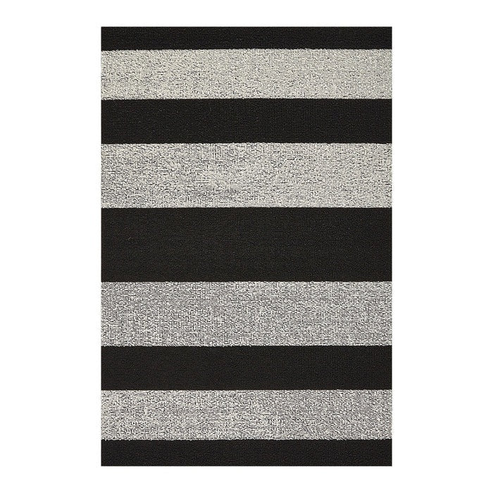The CHILEWICH Black and White Bold Stripe Shag Doormat (18x28) rests on a light floor, with a pair of black flip-flops positioned to the right of the mat. Horizontal white wall panels provide a background.