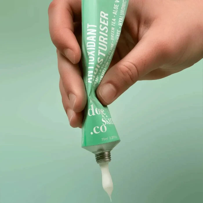 Hand holding a green tube of moisturizer with visible brand name against a light green background