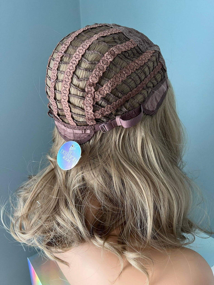 Back view of a short blonde wig cap construction with highlights and adjustable straps.