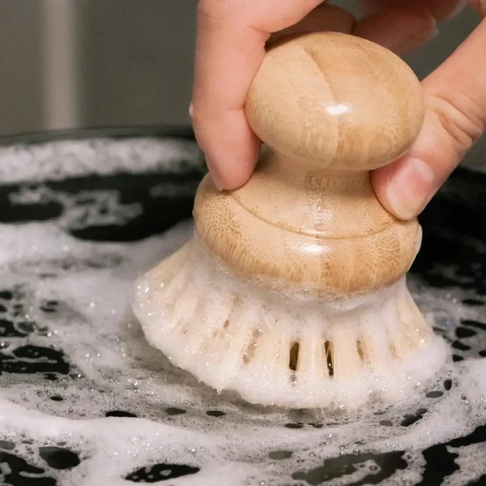 Hand holding a wooden scrubber over a soapy surface