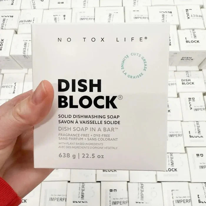 Hand holding a 'No Tox Life' dish block soap bar packaging against a background of similar packaging.