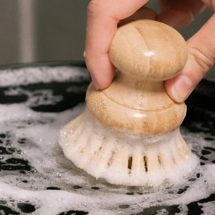 Hand holding a scrubber with wooden handle over a soapy surface