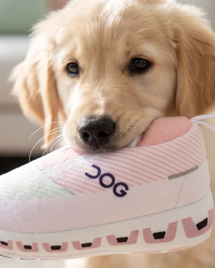 Introducing the DOG WORKOUT SHOE DOG TOY from HAUTE DIGGITY DOG—a plush slipper-shaped toy styled like a pink and white sneaker with "DOG" written on the side, a thick sole, and a handy loop at the back, all designed to mimic a fun workout shoe for playful pups.