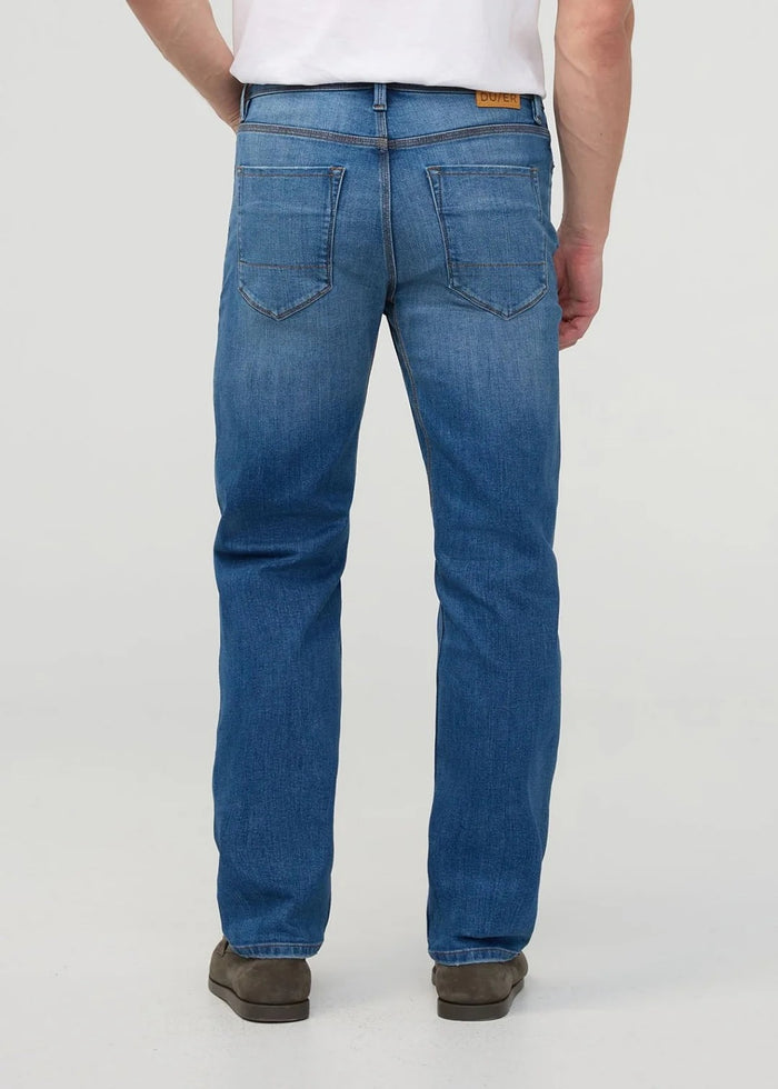 Close-up of a person wearing DUER’s PERFORMANCE DENIM+ Straight Pants in Alpine Indigo, showing relaxed hands and highlighting the texture, stitching, and stretch comfort of these blue jeans against a plain light background.