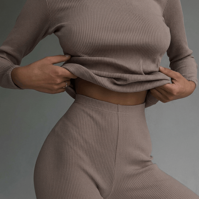 Person wearing a beige ribbed sweater and pants against a gray background