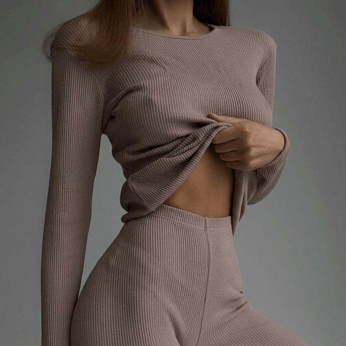 Person wearing a beige ribbed sweater and pants against a gray background
