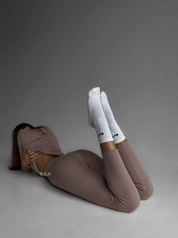 Person wearing brown leggings and white socks lying on a gray background