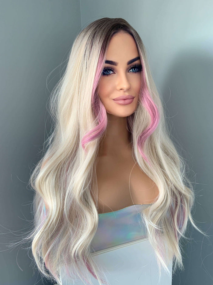 Mannequin head with long, wavy hair featuring blonde and pink coloration against a plain background.