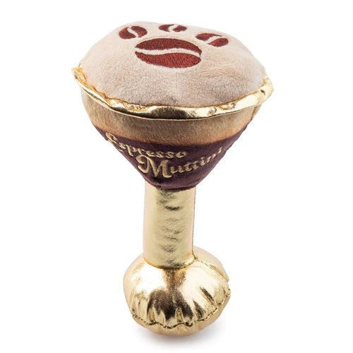 An espresso martini-shaped plush from HAUTE DIGGITY DOG, the ESPRESSO MUTTINI DOG TOY, rests on a marble table beside a coffee cup. This durable dog toy features gold, brown, and cream colors and displays “Espresso Mutini” on the side.