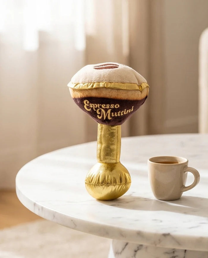 The ESPRESSO MUTTINI DOG TOY by HAUTE DIGGITY DOG is a plush dog toy designed to resemble a martini glass, featuring a gold stem and base, brown “liquid,” and a tan top with a charming paw print detail. "Espresso Mutini" is embroidered on the side, and an engaging squeaker inside ensures hours of fun for your pup.
