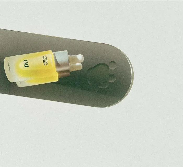 Two bottles of 'Oil' product on a gray surface with a white background