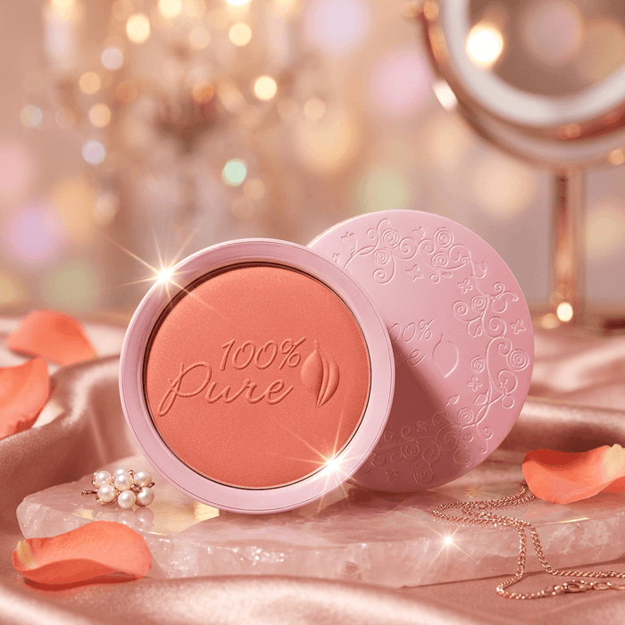 100% Pure blush compact with pink lid on a decorative background with jewelry and flowers.