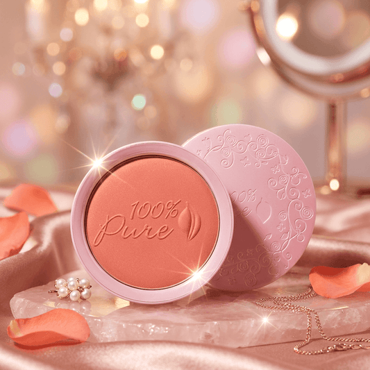 100% Pure blush compact with pink lid on a decorative background with jewelry and flowers.