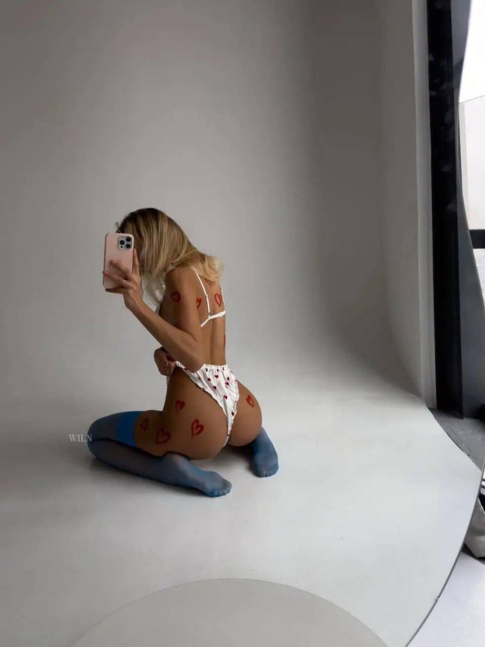 Model showcasing GLAM Stockings Blue with heart designs on skin, posing in stylish underwear on a minimalist set.
