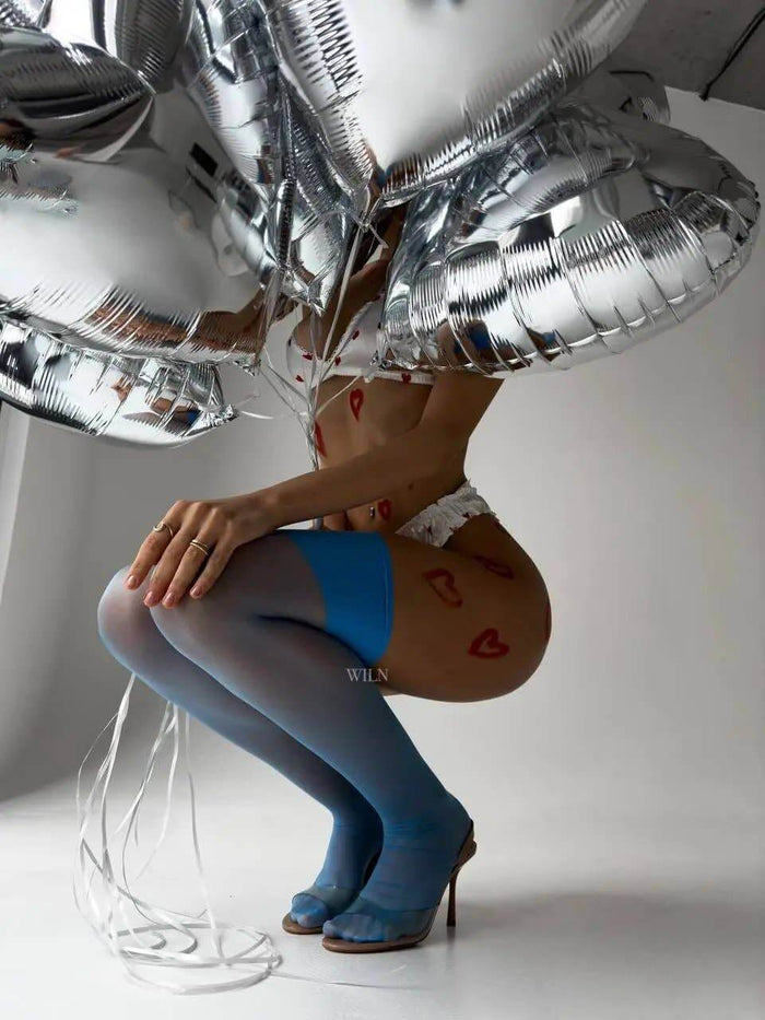 Model wearing GLAM Stockings Blue while holding silver balloons, showcasing elegance and modern fashion style.